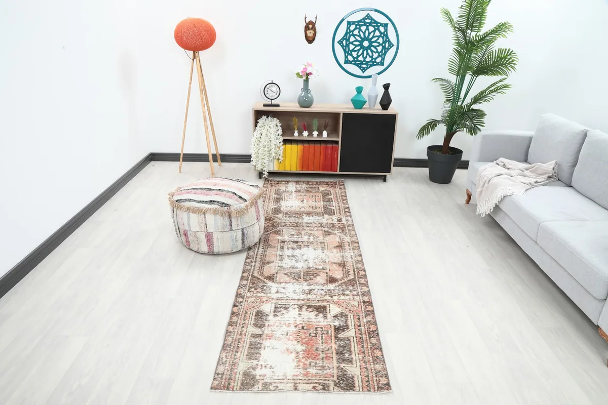 Vintage runner rug in a modern room setting with a sofa and pouf, showing its full length.