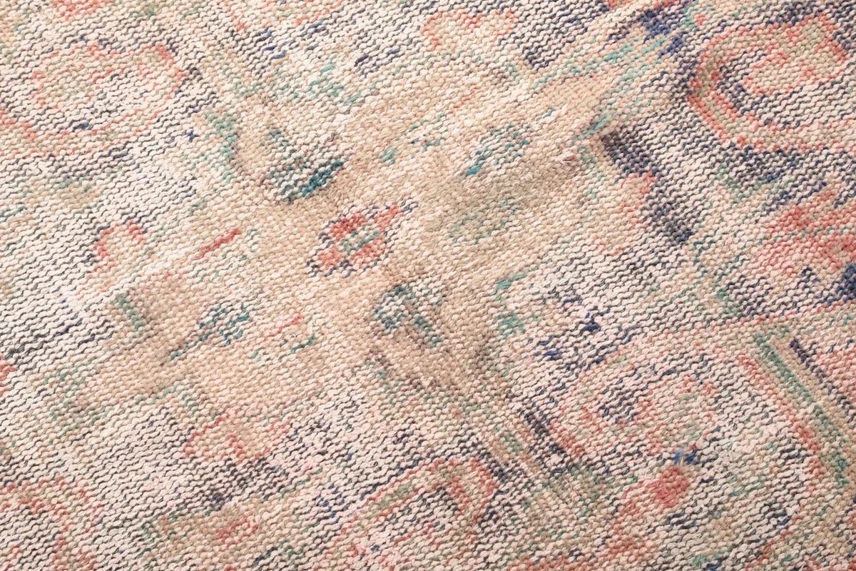 Detailed view of the low wool pile texture and faded colors of the hand-knotted rug.