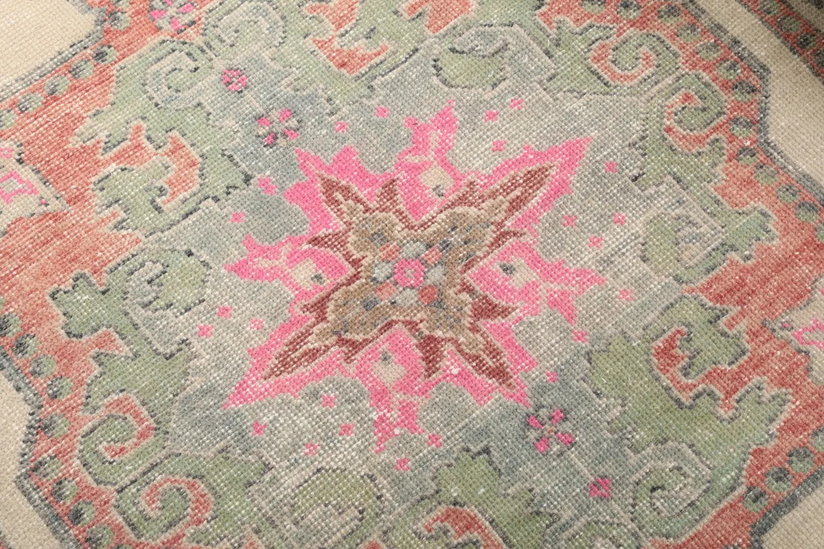 Close-up of the rug's central pink and green medallion, revealing the hand-knotted wool pile and color blending.