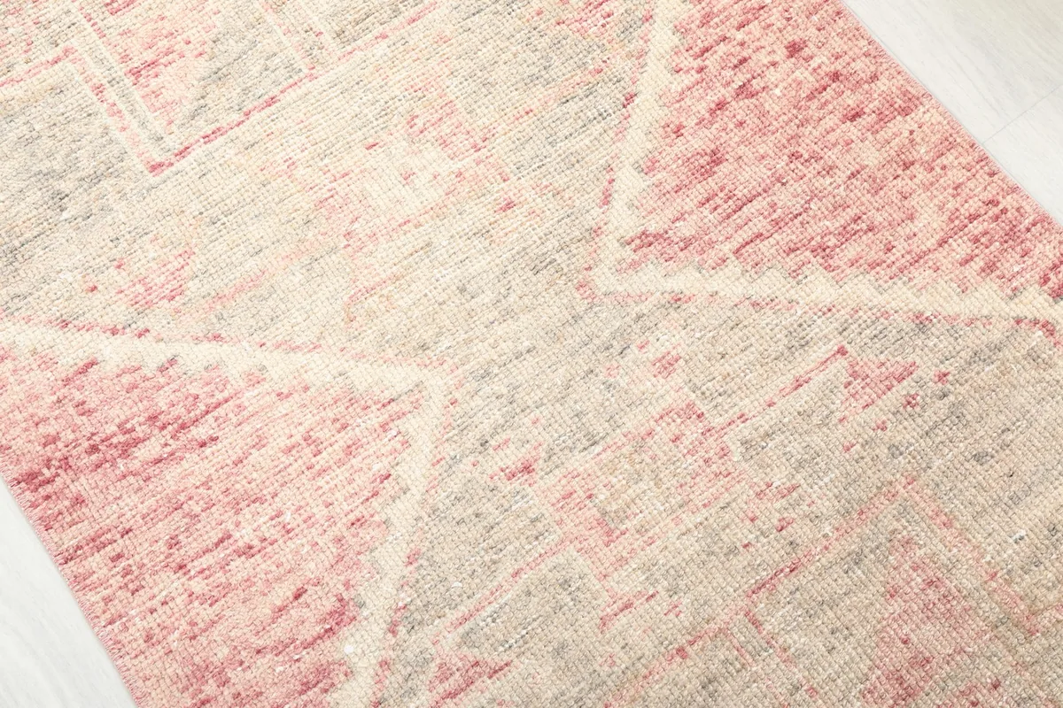Detailed view of the hand-knotted wool pile and the distressed rose and gray coloring of the rug.