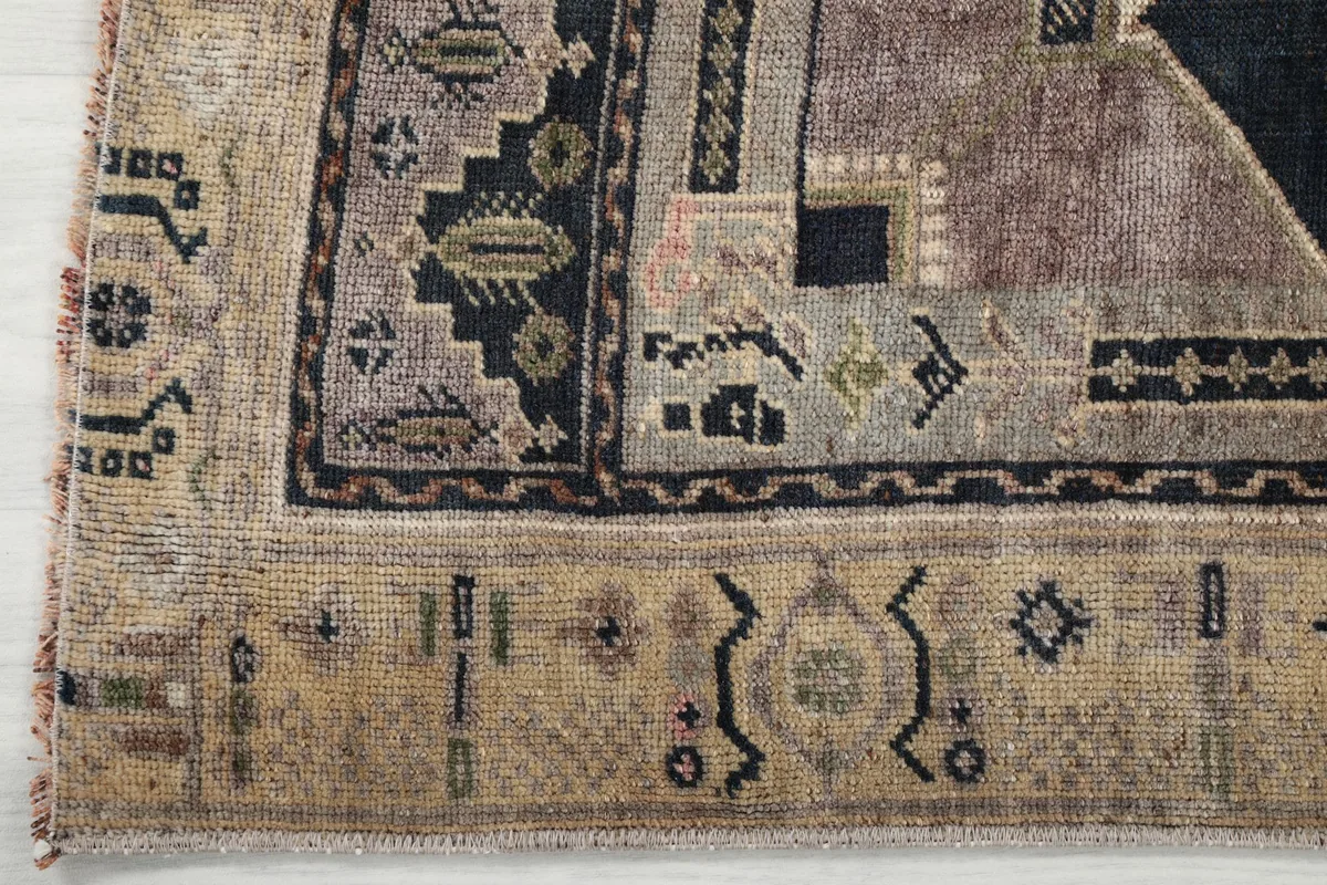 Corner detail of the rug's beige border, showcasing the tribal motifs and the transition to the main field.