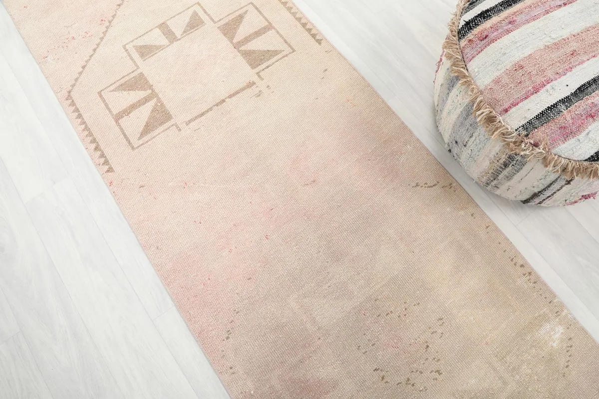 Close-up detail of the rug's surface, revealing the subtle rose beige color and some wear.
