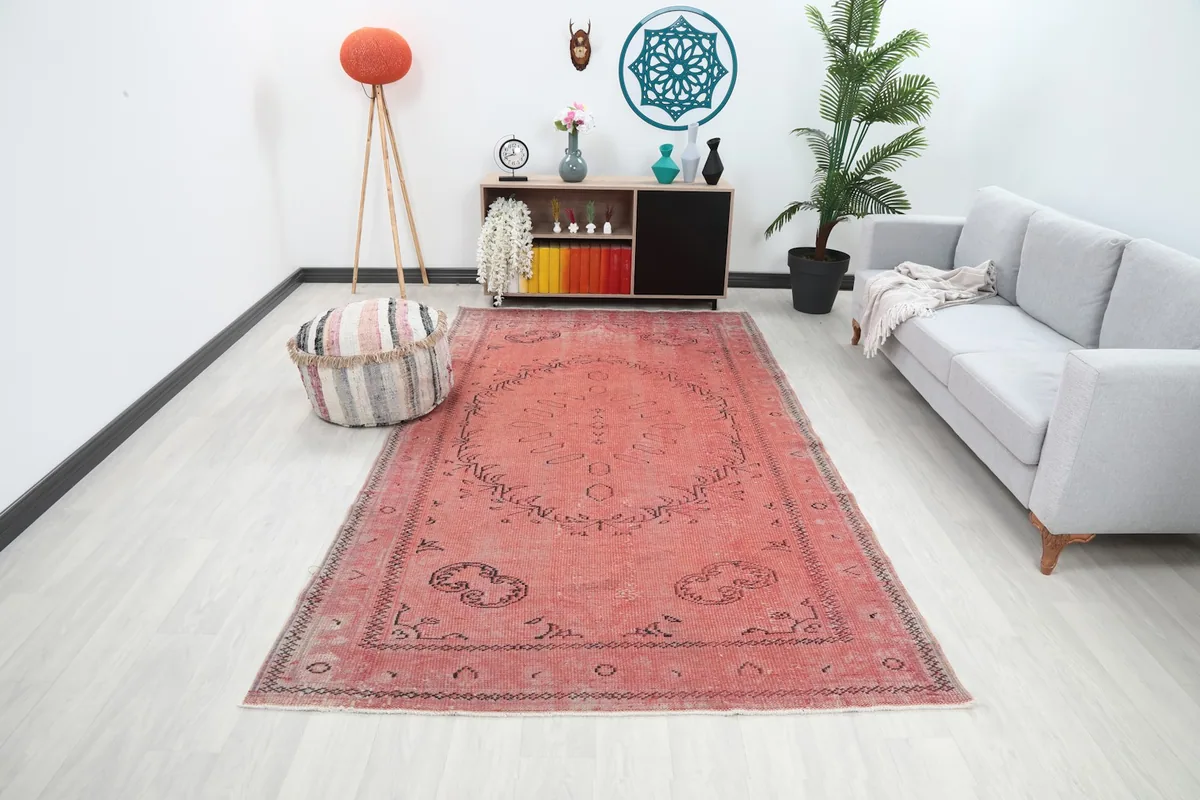 Rose vintage Anatolian rug displayed in a living room setting with a sofa and pouf
