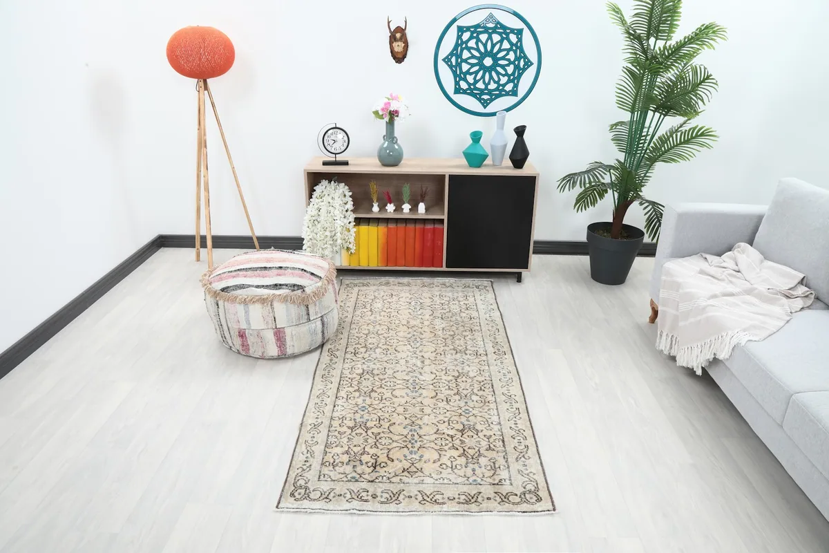 Vintage beige floral rug in a modern living room setting with a sofa and pouf