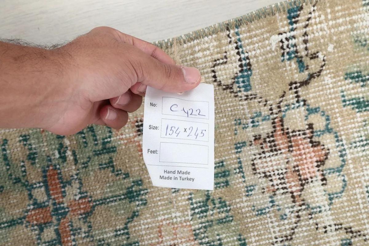 Hand holding a tag showing the rug's dimensions and 'Hand Made in Turkey' on the rug surface