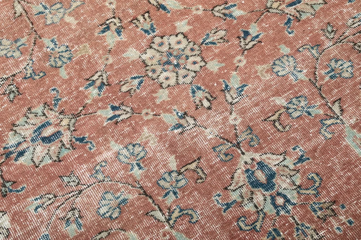 Detailed close-up of the rug's floral motifs in blue and beige against the rust background, showing the low pile.
