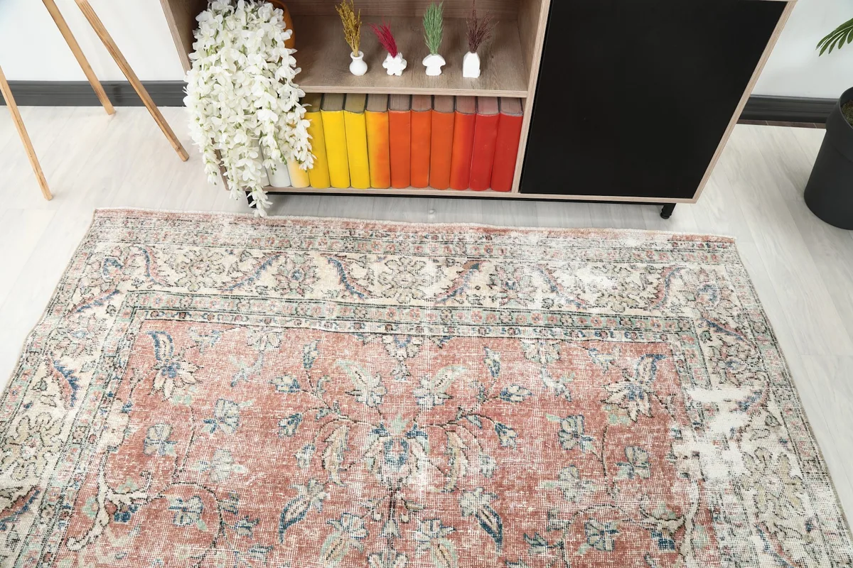Overhead shot of the rug's upper section, showing the beige border and rust field with subtle blue floral patterns.
