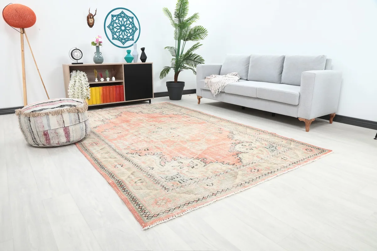 Angle view of the rose and ivory rug in a living space, showing its size relative to a sofa and ottoman