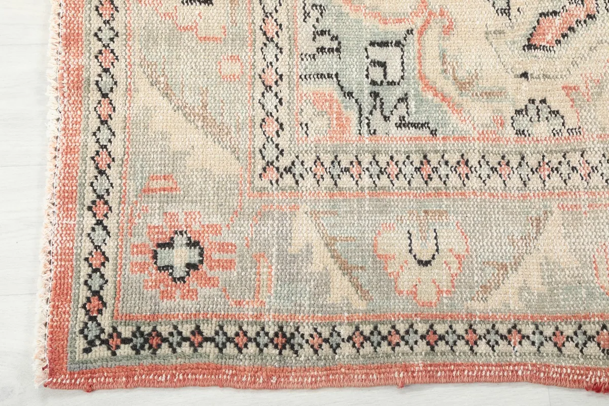 Detailed view of the rug's geometric border and corner, showcasing the gray, rose, and black patterns