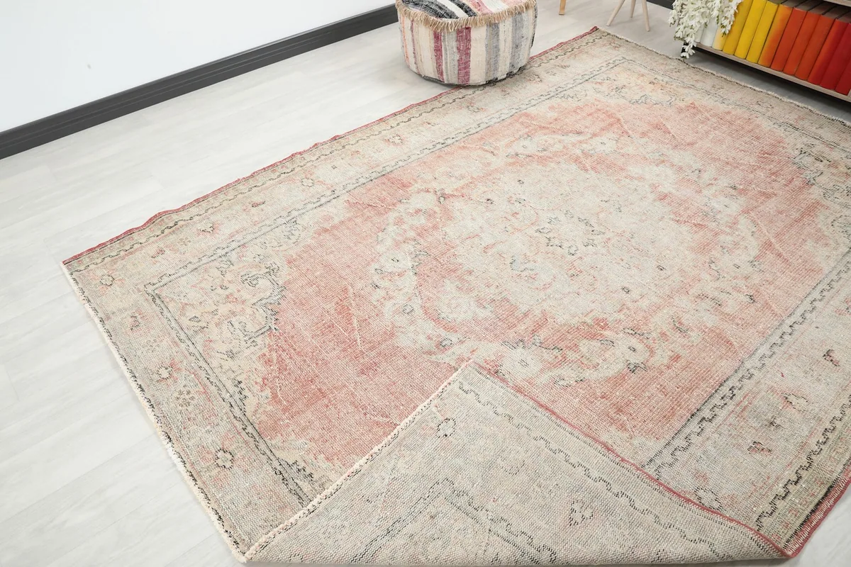 Corner of the rose and beige rug folded back, showing the back of the weave and texture