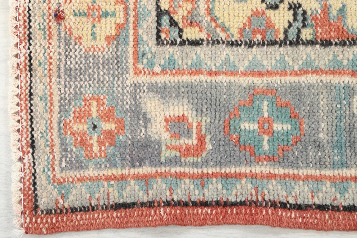 Close-up of the rug's outer border, displaying geometric patterns in gray, rust, and blue tones.