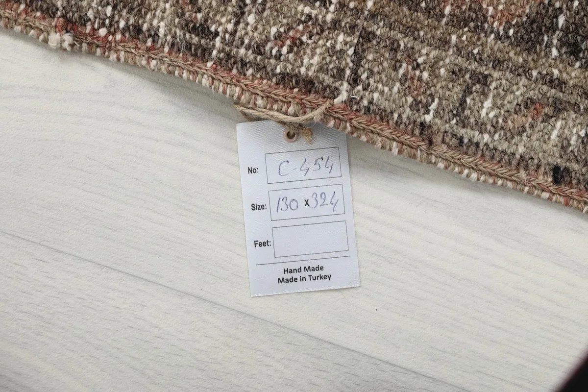 Care tag attached to the rug, detailing its handmade origin and dimensions in cm