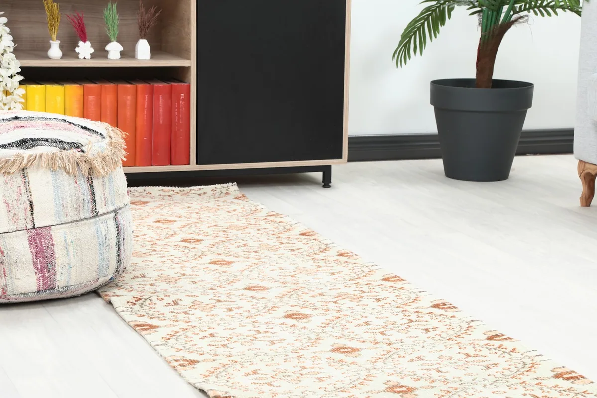 Close-up perspective of the runner rug on the floor next to a patterned ottoman and a dark cabinet.