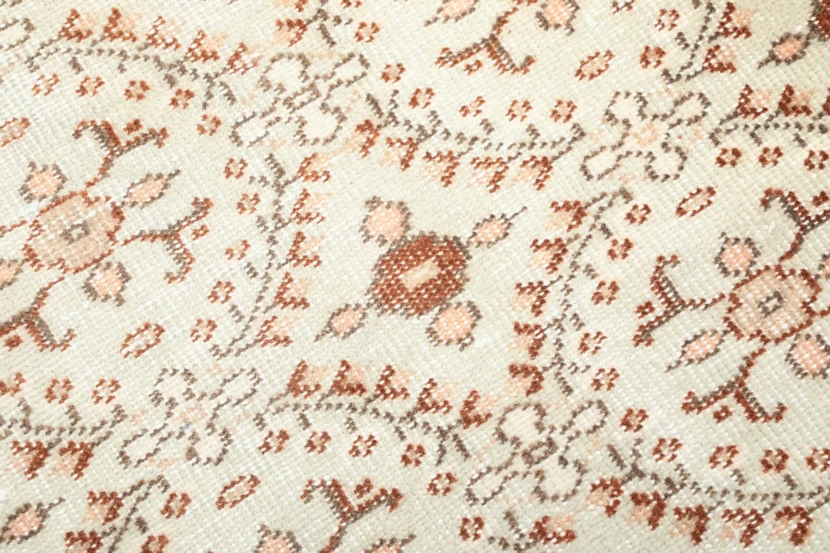 Close-up detail of the hand-knotted wool pile and the intricate ivory, rust, and pink geometric floral pattern.