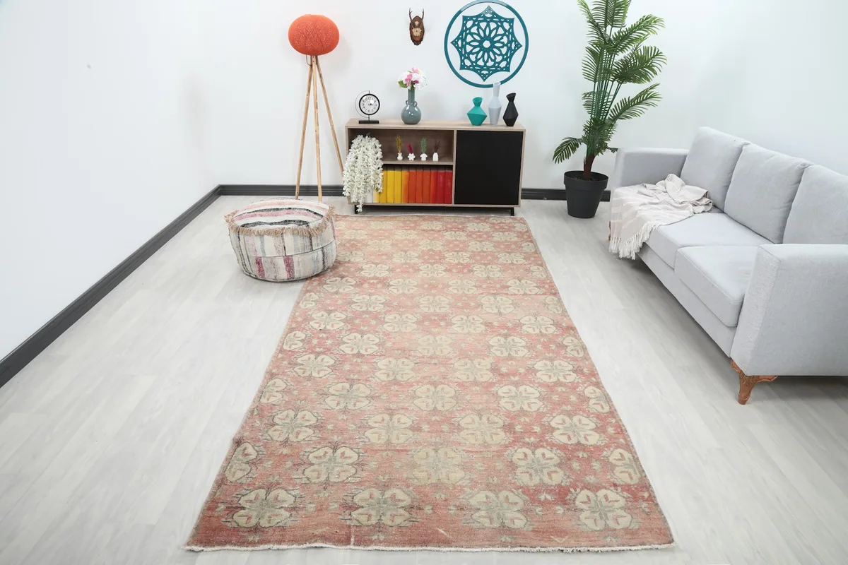 Vintage Anatolian area rug with rose and beige geometric pattern displayed in a modern living space with a gray sofa.