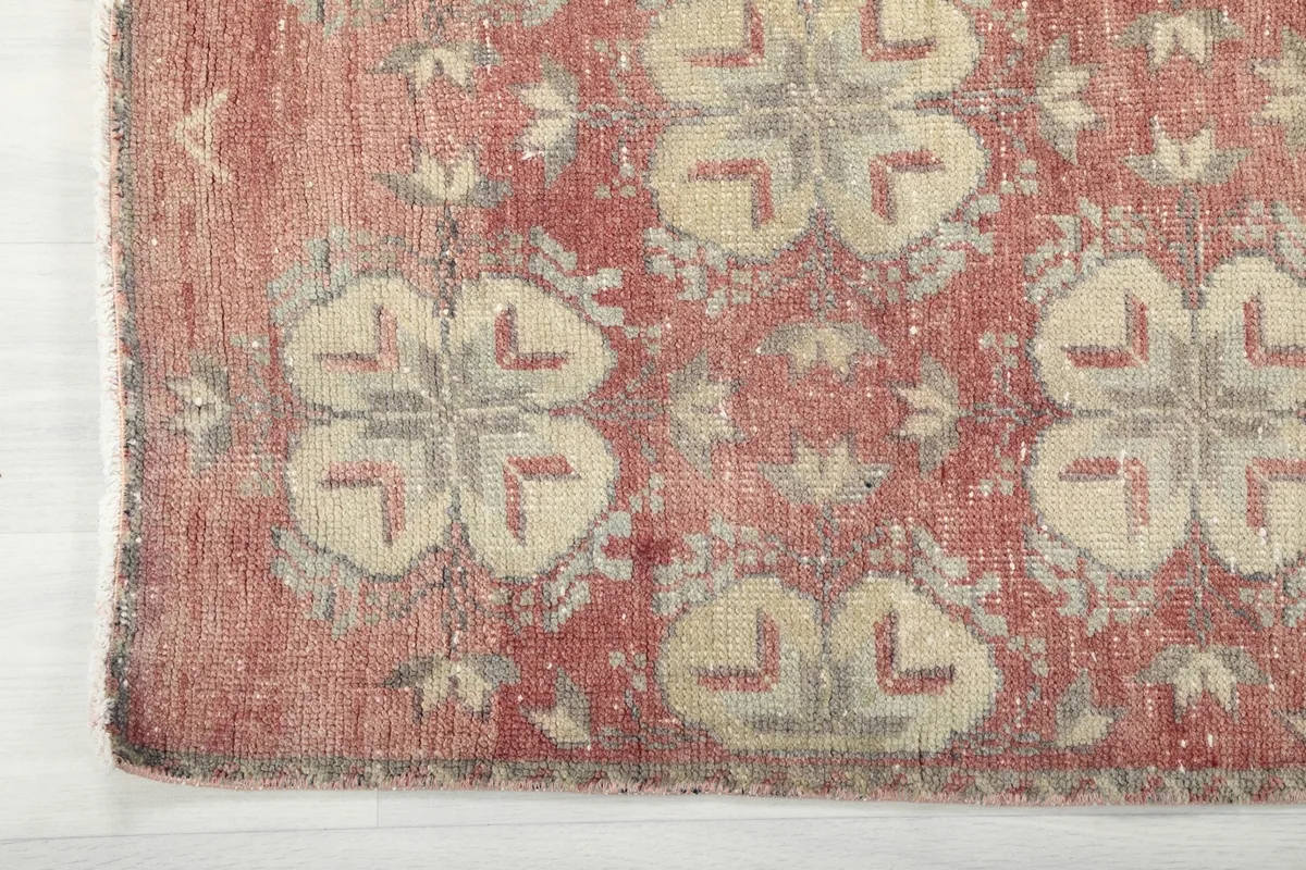 Corner detail of the rose geometric rug, showing the faded edge and hand-knotted construction.