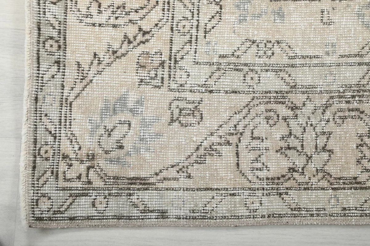 Corner detail of the rug's tan border with geometric motifs and the gray field.