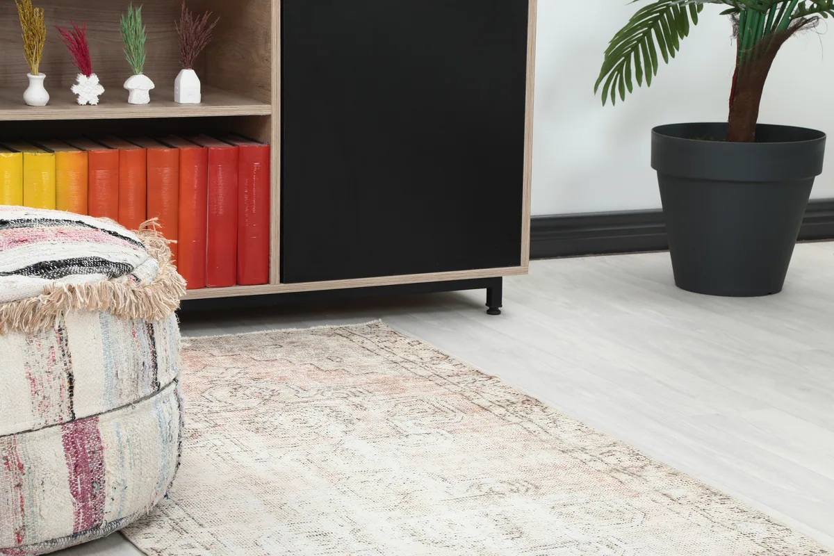 Close-up of the Faded Beige Geometric Medallion Runner in a room, next to a pouf and bookshelf.