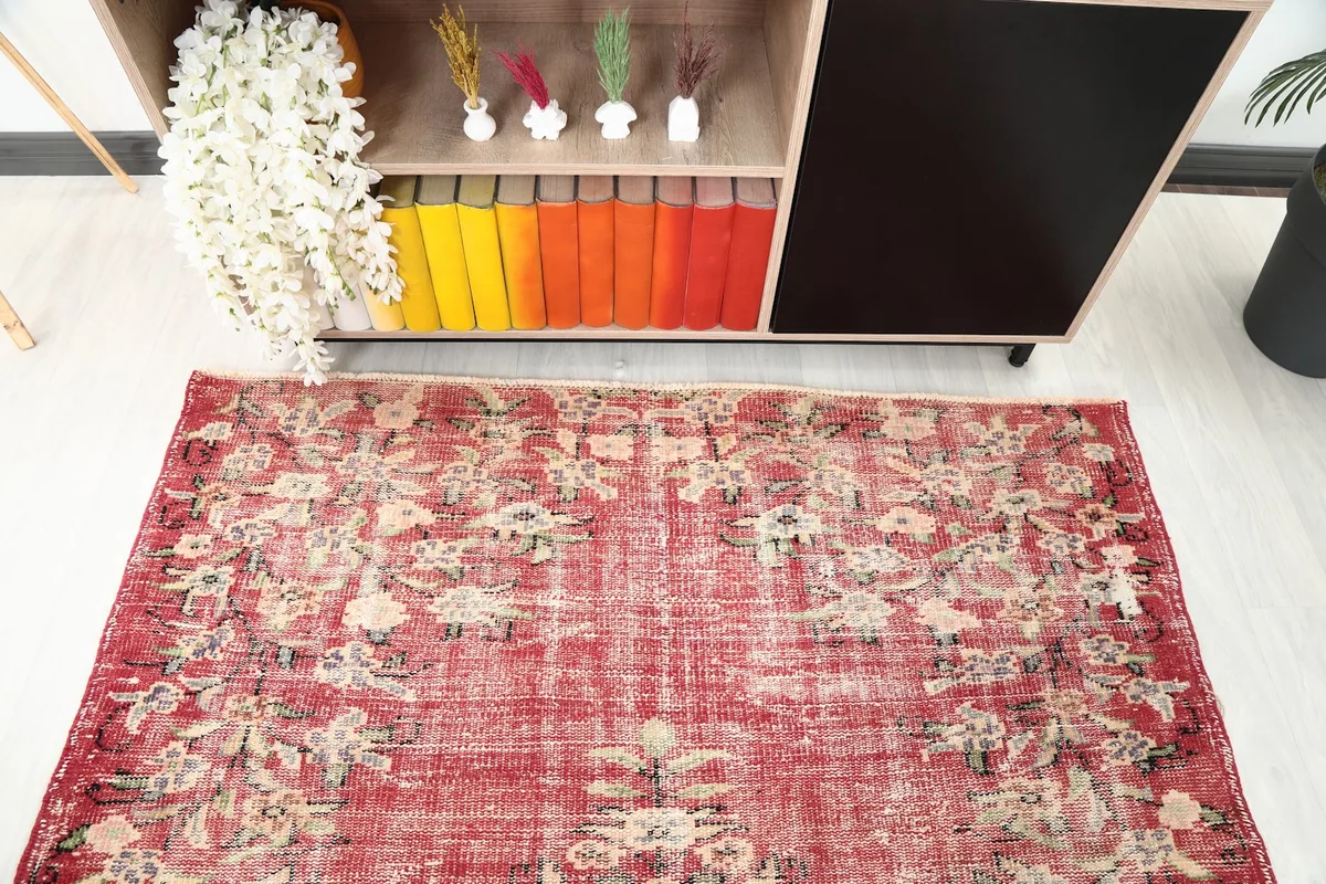 Angled overhead view of the red vintage rug in a room, highlighting its distressed floral pattern