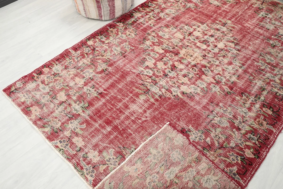 View of the red vintage rug with a corner folded back, showing the pile and cotton foundation
