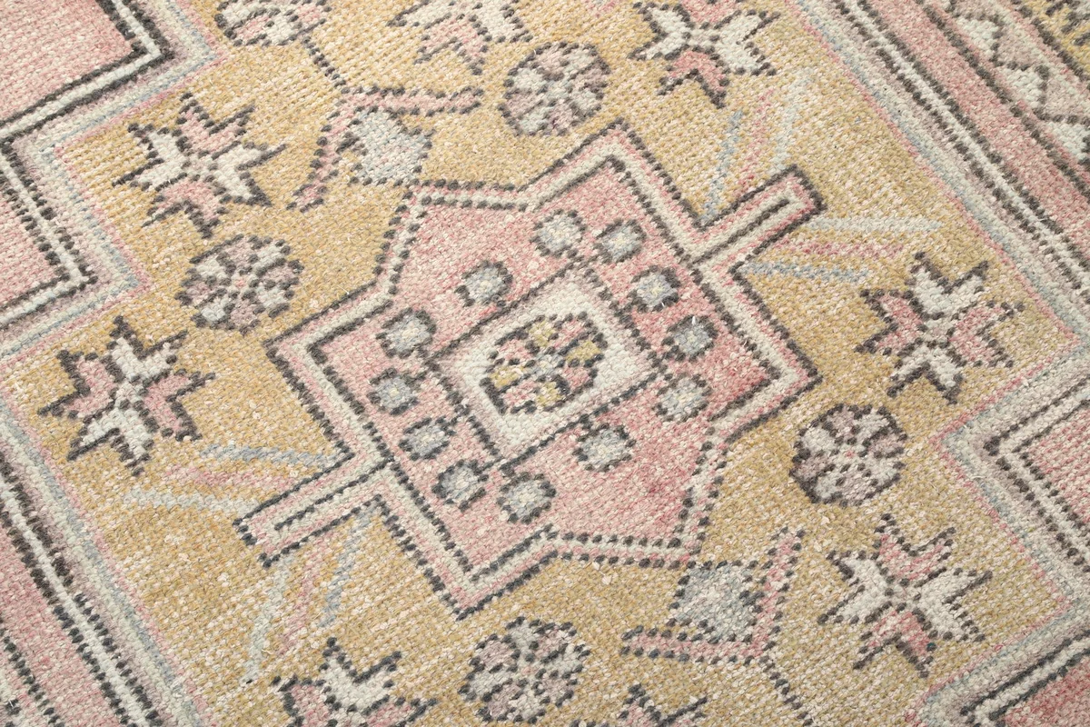 Close-up of the hand-knotted wool pile and intricate geometric motifs in pink, gold, and gray on the rug.