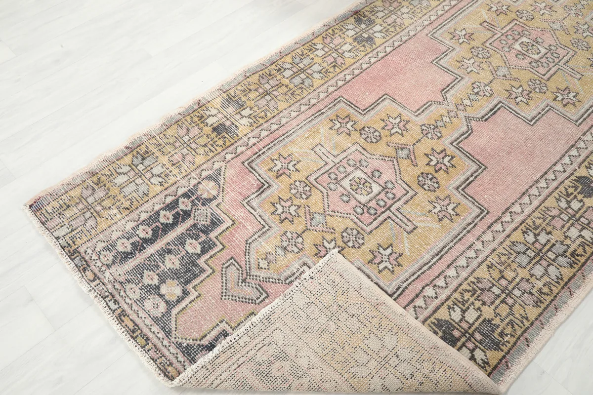 Angled view of the Pink Gold Geometric Anatolian Rug with a corner folded back, showing the back of the rug.