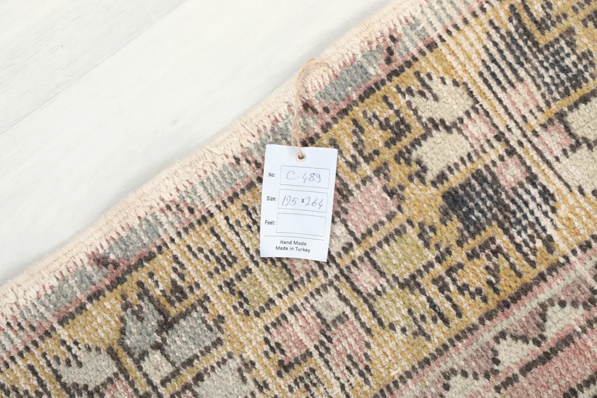 Corner of the Pink Gold Geometric Anatolian Rug with a tag displaying its dimensions and origin.