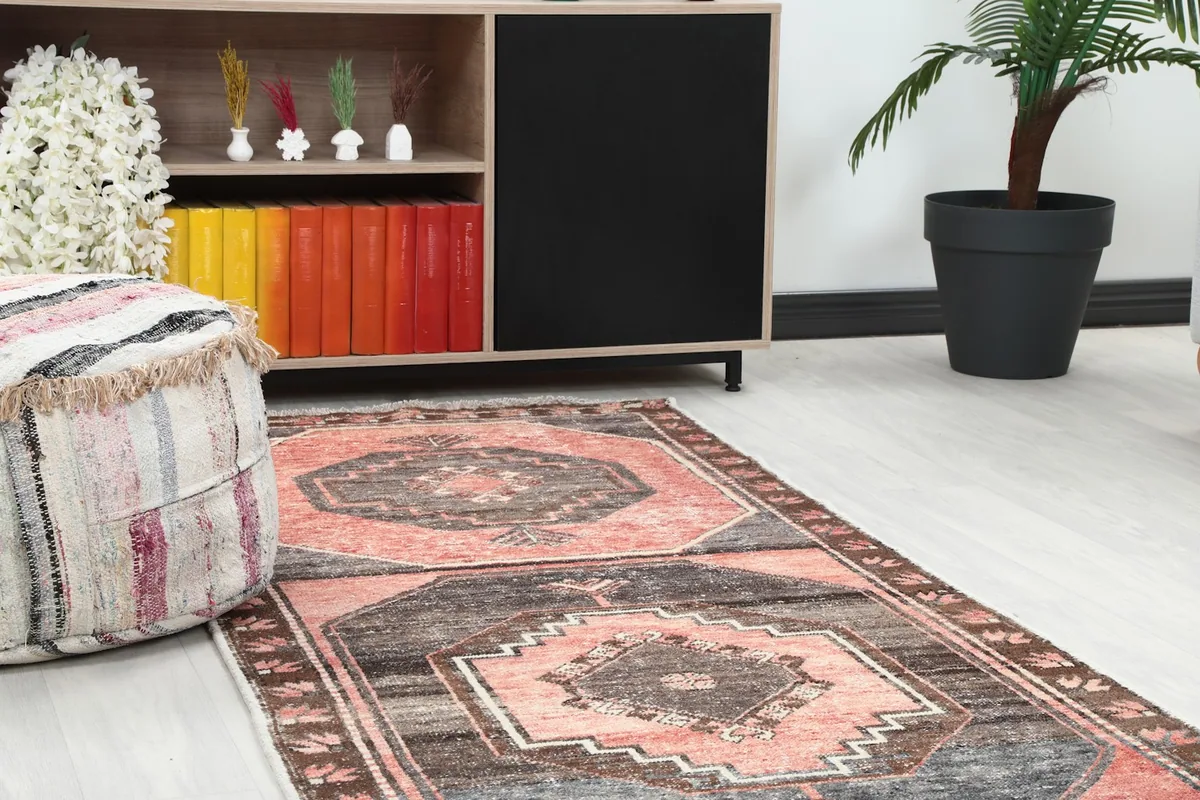 Close-up of the rose and charcoal runner rug's pattern on the floor next to a wooden cabinet and ottoman.