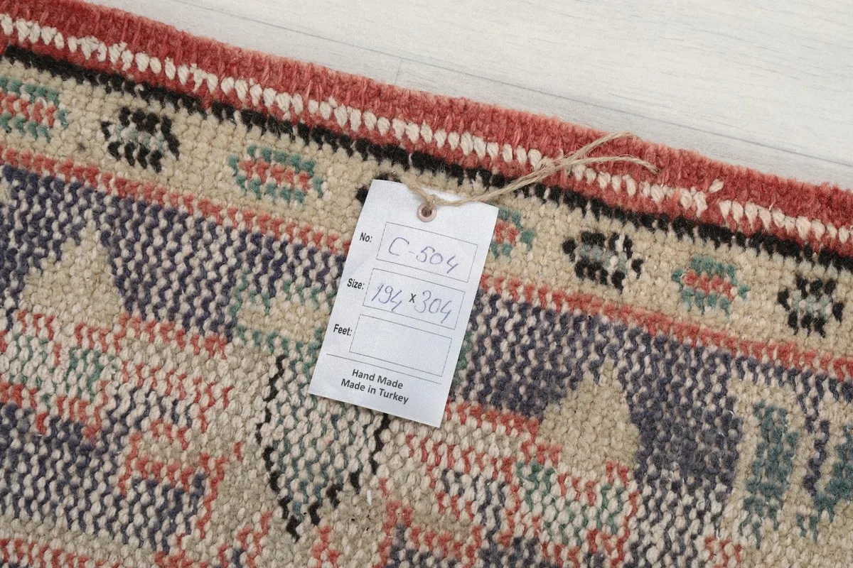 Close-up of the rug's corner with the product tag, indicating its handmade origin and dimensions (194x304 cm).