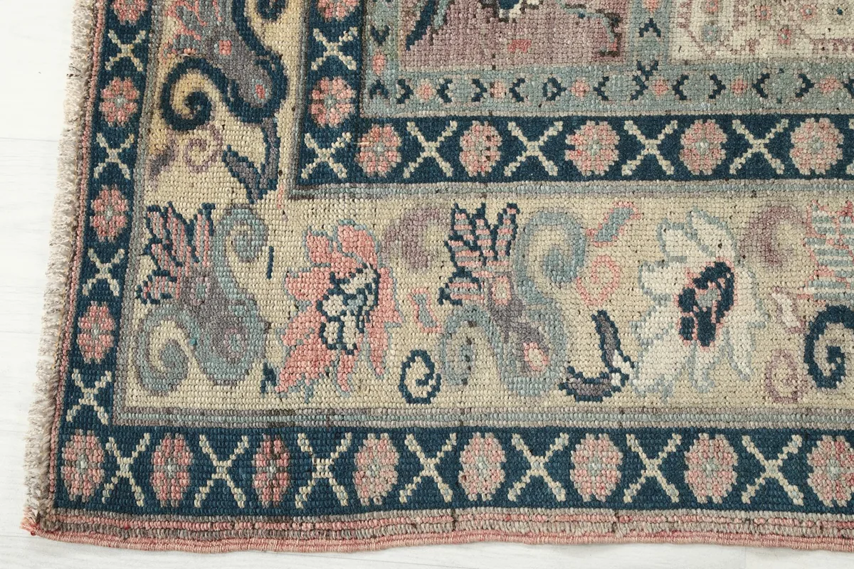 Detailed view of the rug's border, showcasing floral and geometric elements in cream and pink