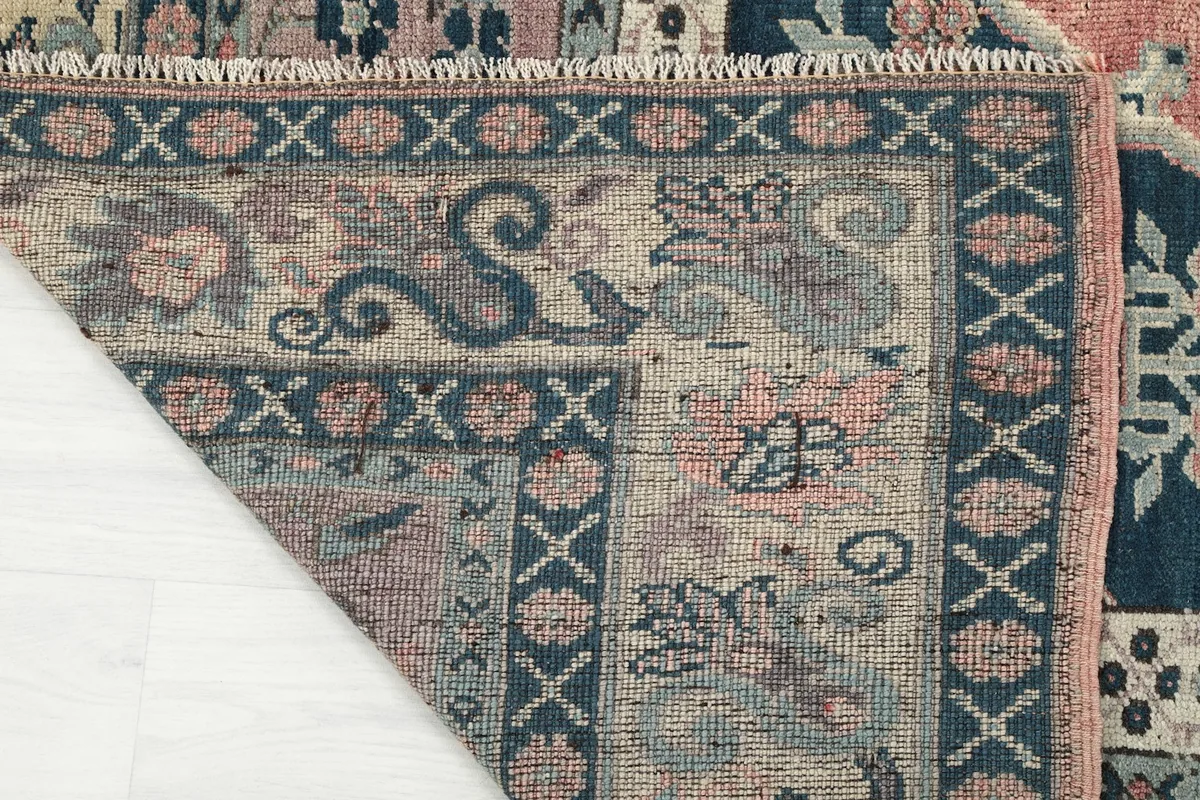 Corner of the rug folded back, revealing the hand-knotted construction and fringe