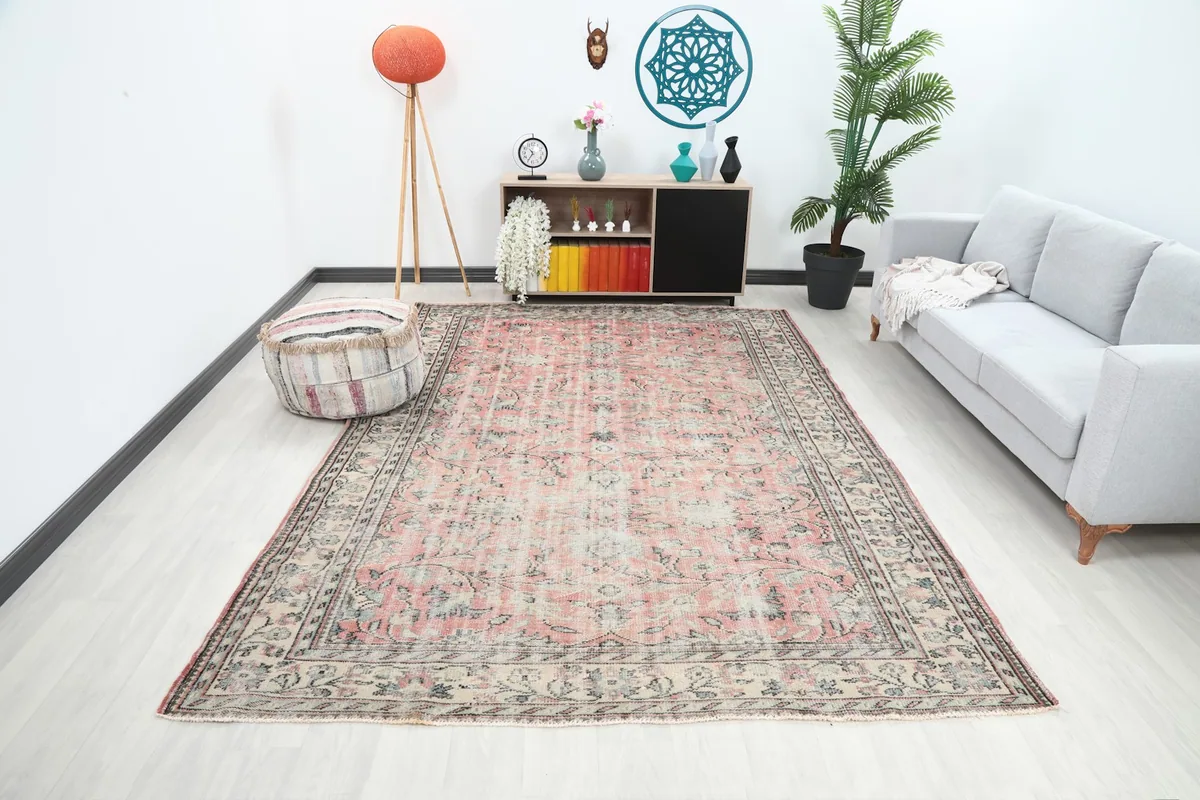 Wide shot of the large rose and ivory vintage rug placed in a modern living room setting with a gray sofa.