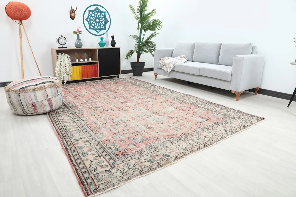 Angled view of the rug in a living room, showing the faded rose field and detailed ivory border alongside furniture.
