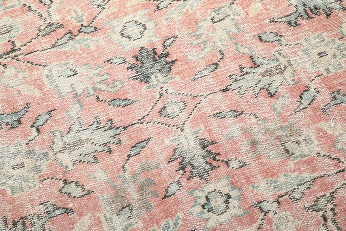Close view of the hand-knotted wool pile, showing individual knots and the distressed appearance of the floral pattern.