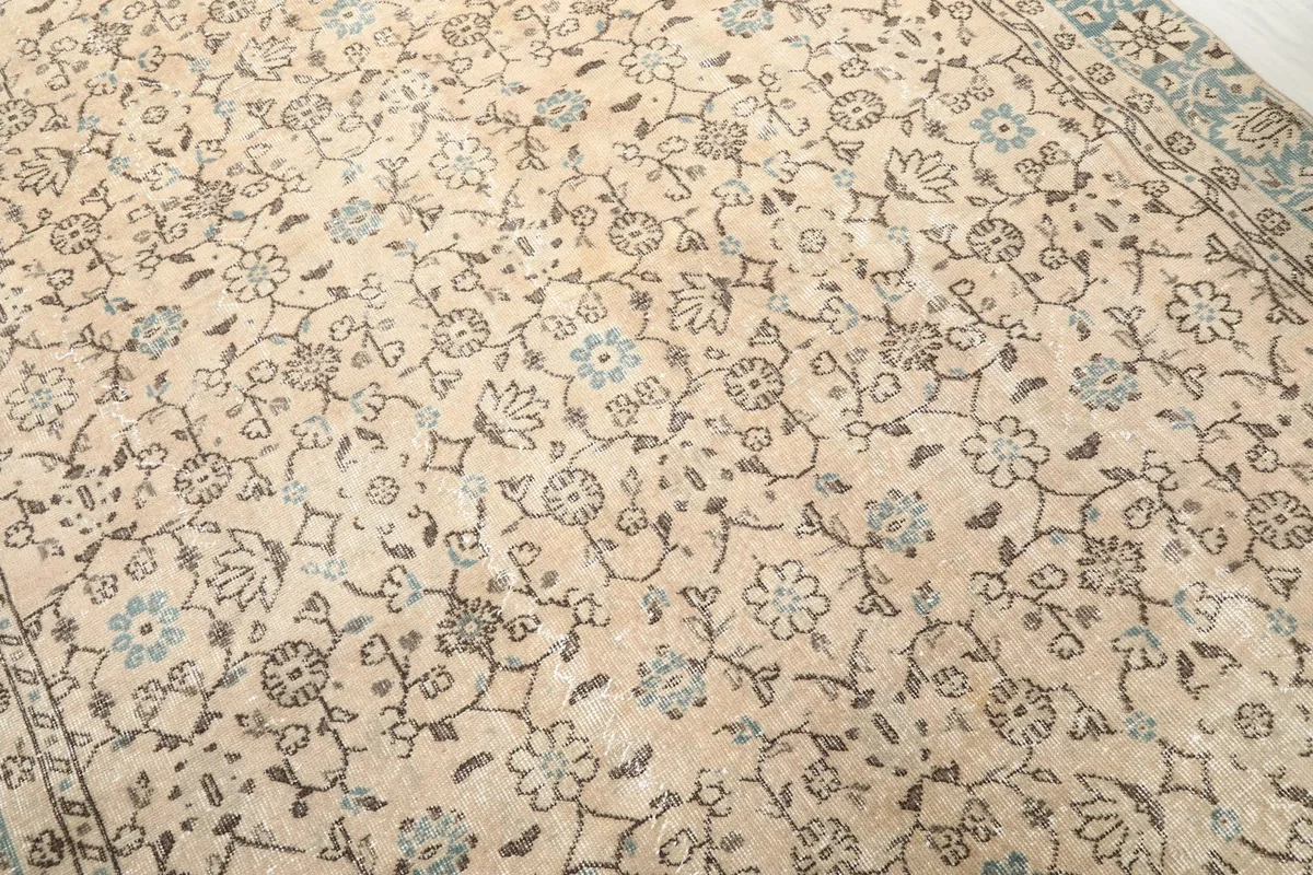 Detailed view of the rug's central floral pattern, showing the beige field and brown and blue motifs.