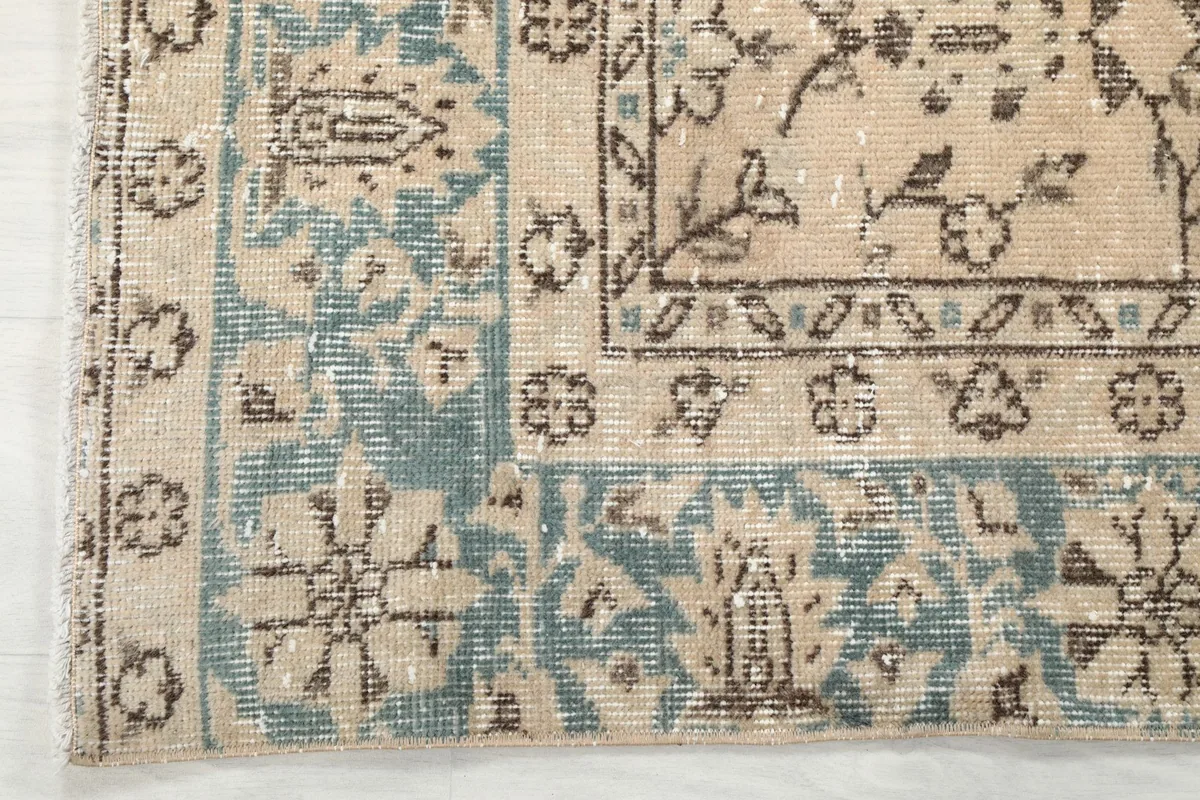 Corner detail of the rug, showcasing the blue border and the transition to the beige field.