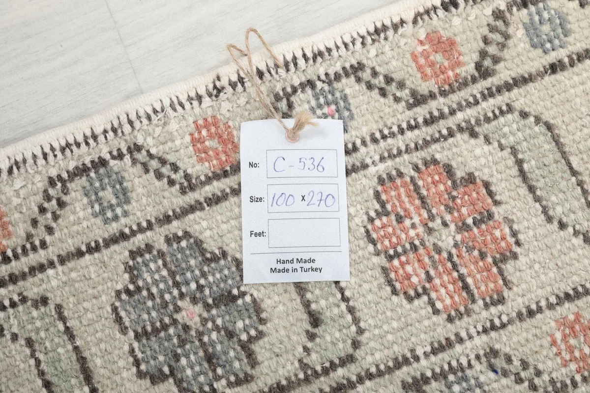 Close-up of the rug's pattern with a product tag displaying 'Hand Made in Turkey' and size '100 x 270 cm'.