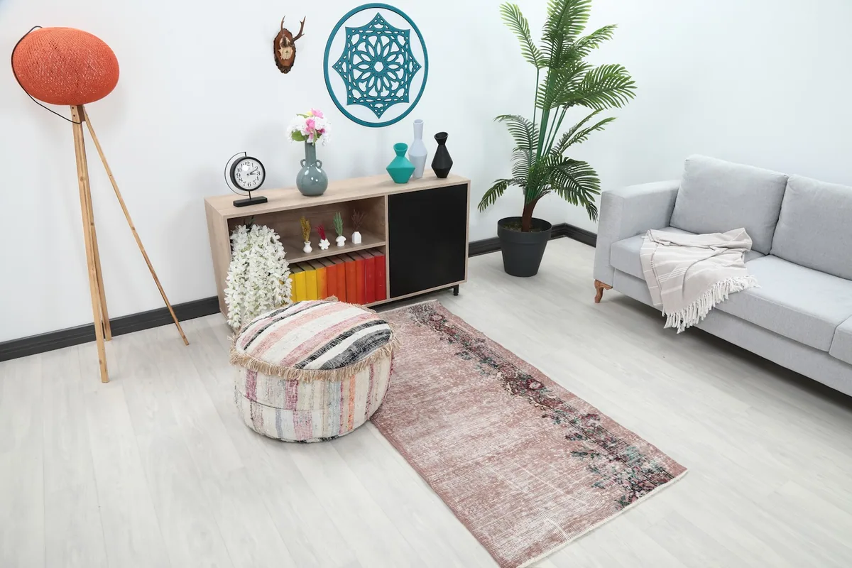 Angle view of the rose wool rug in a living space, showing its placement relative to a pouf and sofa