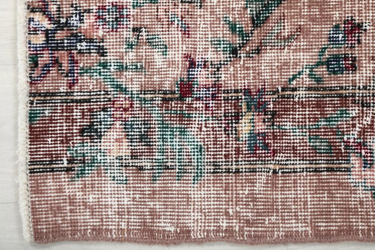 Detail of the rug's floral border, highlighting the green, blue, and red hues against the rose field