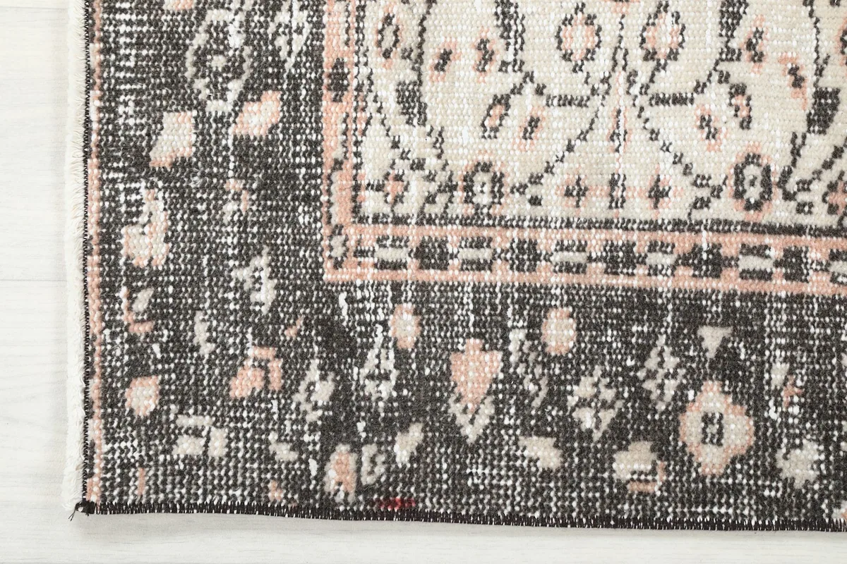 Corner detail of the rug, showcasing the charcoal border with its intricate patterns and rose accents.