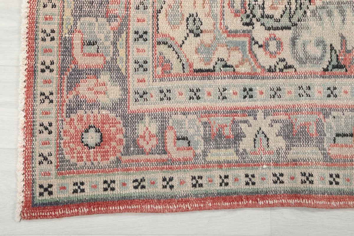 Close-up of a corner of the rug, showing the detailed geometric patterns in the gray and rose borders