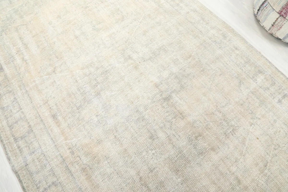 Close-up showing the subtle faded geometric pattern and texture of the ivory and gray rug
