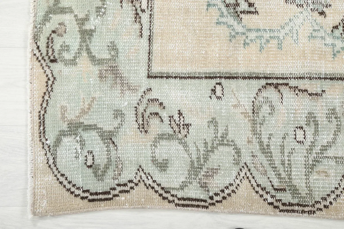 Detail of the rug's green border with its scalloped edge and geometric patterns.