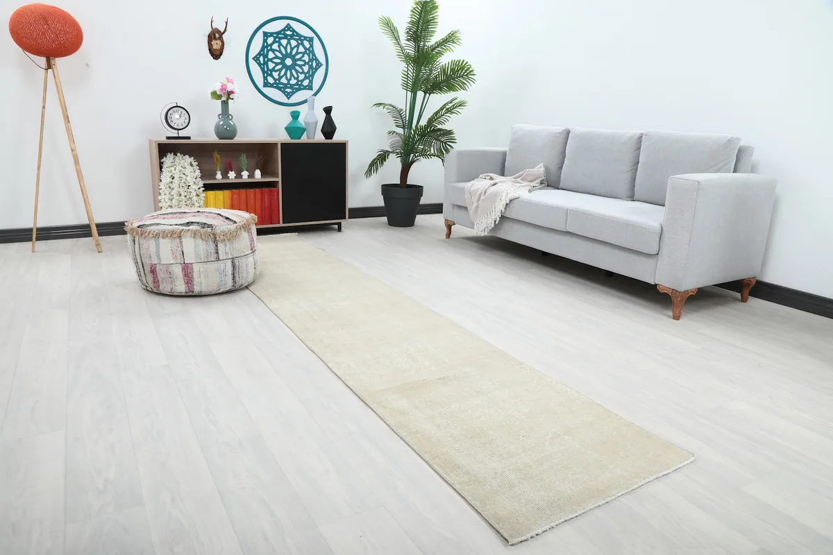 Angle view of the cream runner rug in a room setting, highlighting its long, narrow shape and subtle texture.