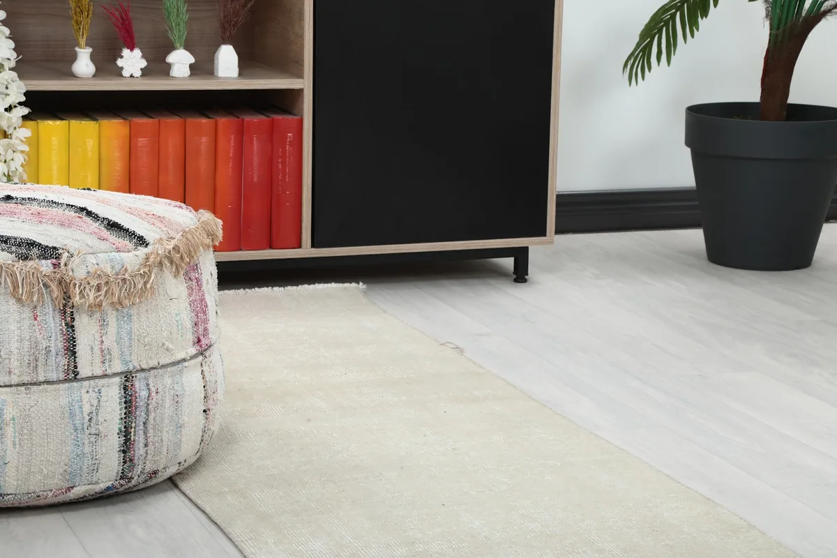 Close-up view of the cream runner rug's texture and color variation next to a decorative ottoman.