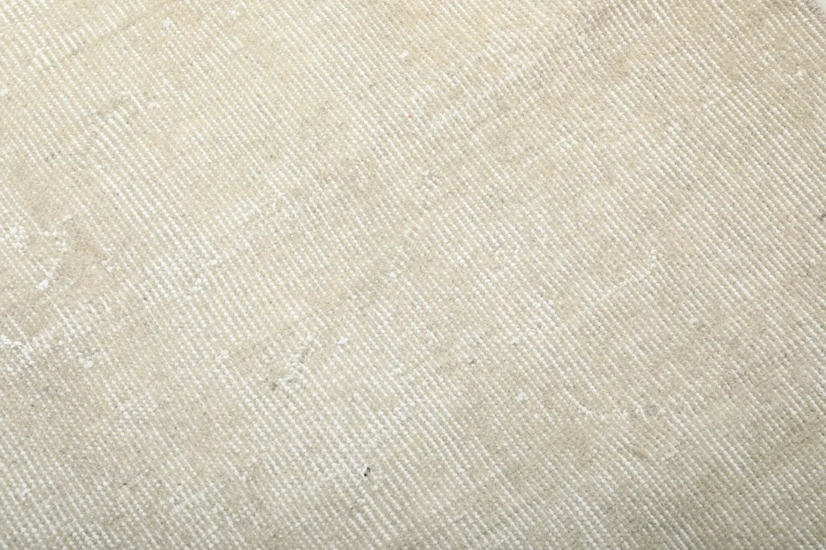 Detailed close-up showing the low wool pile and the subtle distressed appearance of the cream rug surface.