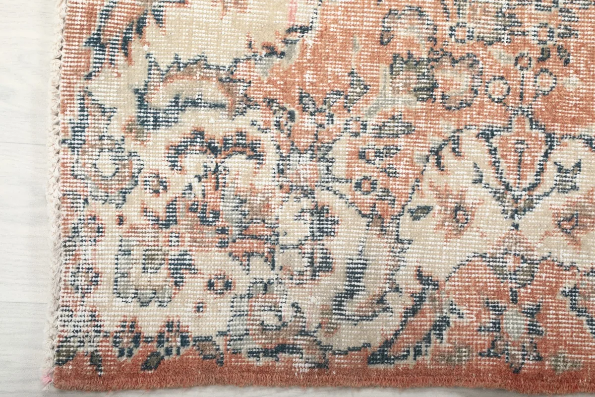 Detailed view of the rug's outer border and corner, with faded rust and blue motifs.