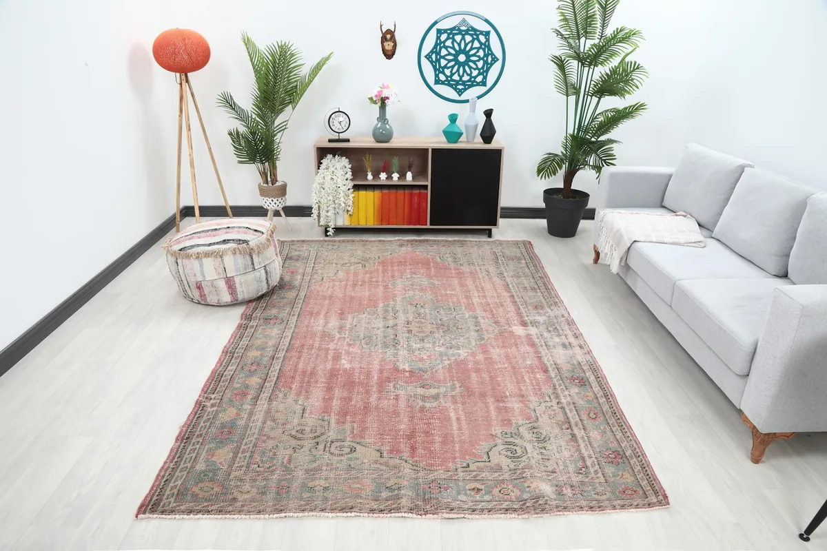 Vintage rose and gray rug displayed in a bright living room setting with a sofa and cabinet