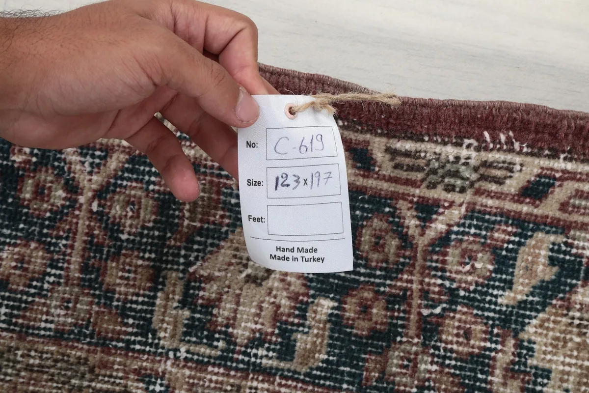 Hand holding a tag indicating the rug's origin as hand-made in Turkey and its dimensions.