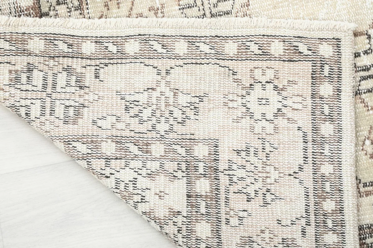 Corner of the rug folded back, revealing the hand-knotted cotton foundation and fringe
